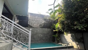 Una piscina con una escalera que sube hacia un edificio, rodeada de follaje.