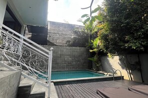 Ein Schwimmbecken mit einer Treppe, die zu einem Gebäude führt, umgeben von Grünpflanzen.