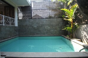 A rectangular swimming pool with a tiled edge, surrounded by a stone wall and a metal railing. - Graca Residence (Badung)