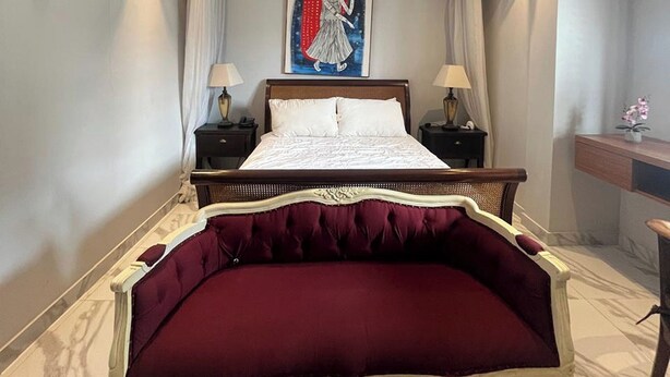 Habitación de hotel con una cama grande, dos mesitas de noche con lámparas, un cuadro en la pared y un escritorio con una planta.