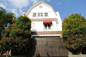 A two-story building with a red awning, a balcony with white railings, and a large metal gate. - Graca Residence (Badung)