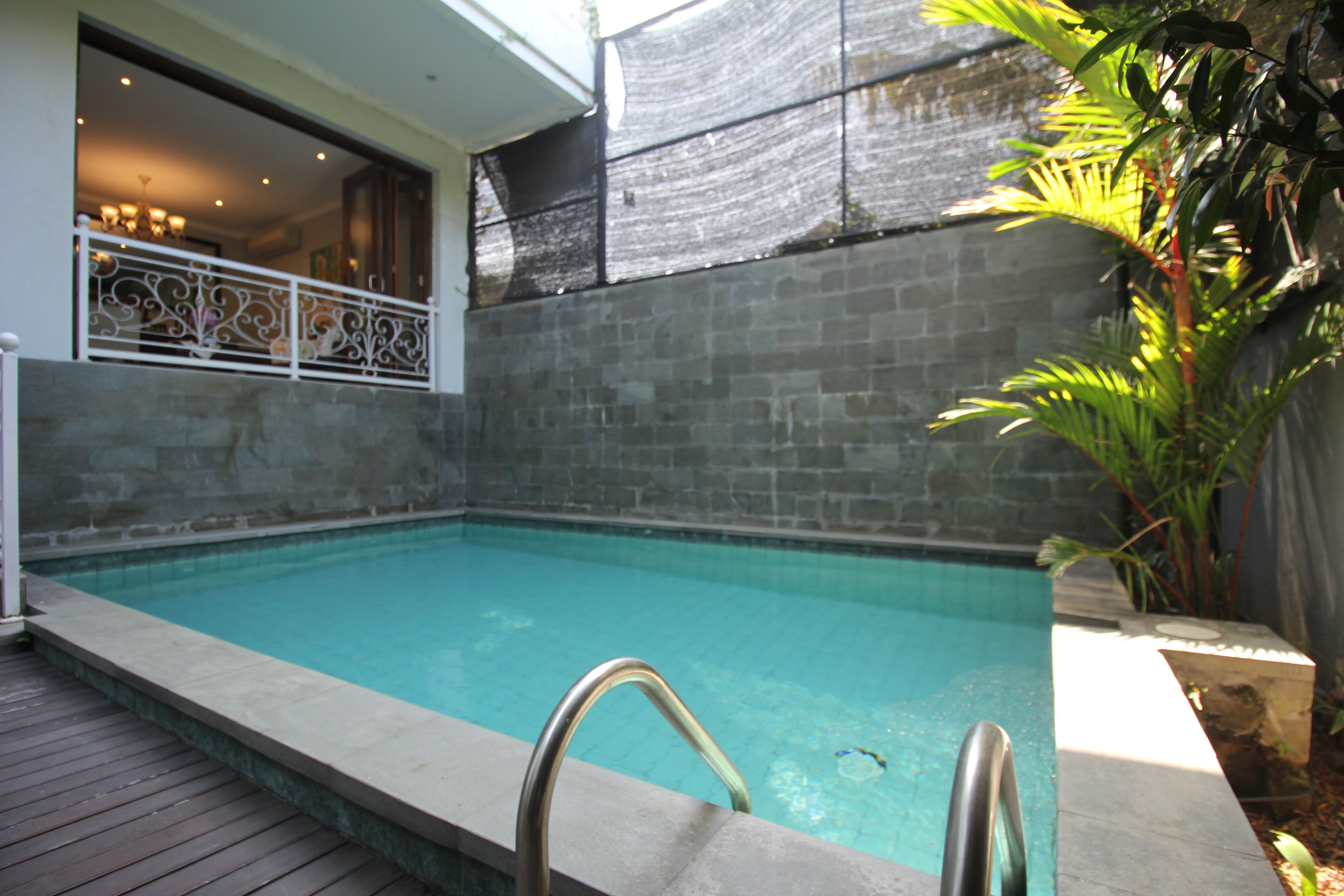 A swimming pool with a metal ladder, surrounded by a stone wall and a wooden deck.