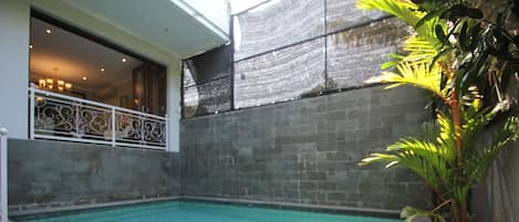 A swimming pool with a metal ladder, surrounded by a stone wall and a wooden deck.