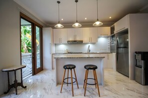 A modern kitchen with a marble countertop, stainless steel appliances, and pendant lighting. - Graca Residence (Badung)