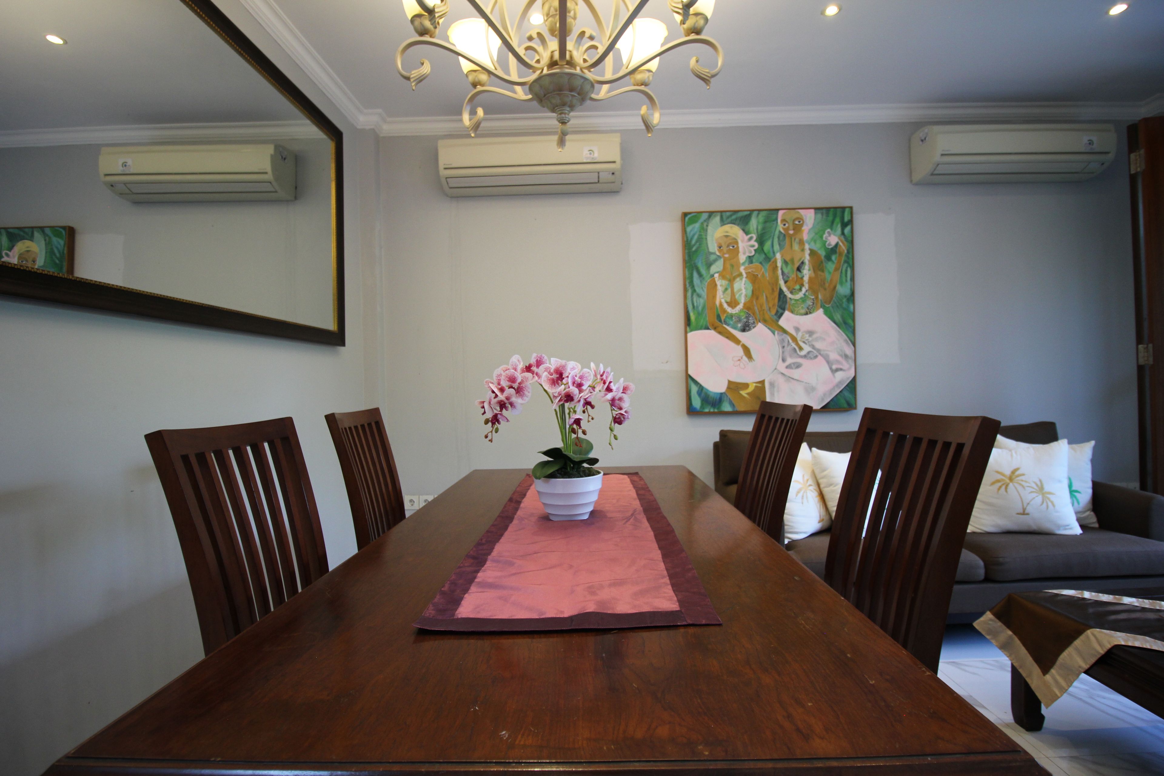 Un coin repas avec une longue table en bois, des chaises, une orchidée en pot et un tableau accroché au mur.