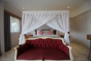 A four-poster canopy bed with a red upholstered headboard, white drapes, and two decorative pillows. - Graca Residence (Badung)