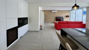 Een moderne keuken met witte kastjes, een inbouwoven en een eethoek met een bank en tafel.