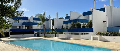 Un bâtiment moderne doté d’une piscine, avec un ciel d’un bleu éclatant et une pelouse bien entretenue.