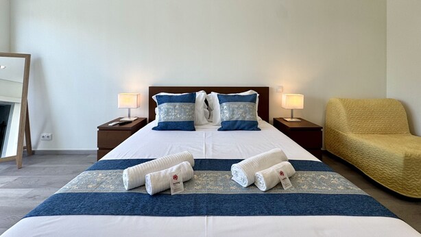 Een hotelkamer met een bed, twee bedlampen, een stoel en twee opgerolde handdoeken op het bed.