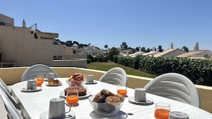 A dining table set with breakfast items, outdoor chairs, and a clear view of a residential area with houses and a tower. - VILAMOURA GOLF VILLA 4 WITH POOL by HOMING (Vilamoura)