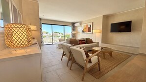 Uma sala de estar moderna com um sofá, cadeiras, uma mesa de centro e uma TV fixada na parede.
