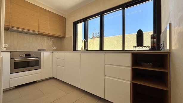 Cozinha com armários brancos, forno embutido e janela com vista para um edifício.