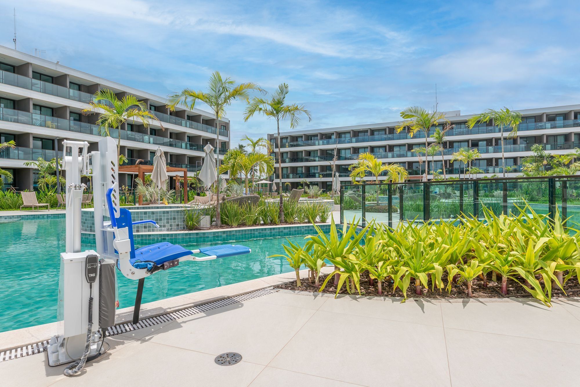 A swimming pool with a lifeguard stand and lounge chairs, surrounded by palm trees and a modern building in the background.
