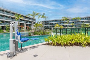 A swimming pool with a lifeguard stand and lounge chairs, surrounded by palm trees and a modern building in the background. - Beachclass Verano Muro Alto (Ipojuca)