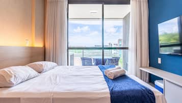 A hotel room with a bed, a TV, a desk, and a view of the city.