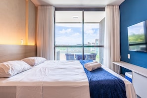 A hotel room with a bed, a TV, a desk, and a view of the city. - Beachclass Verano Muro Alto (Ipojuca)