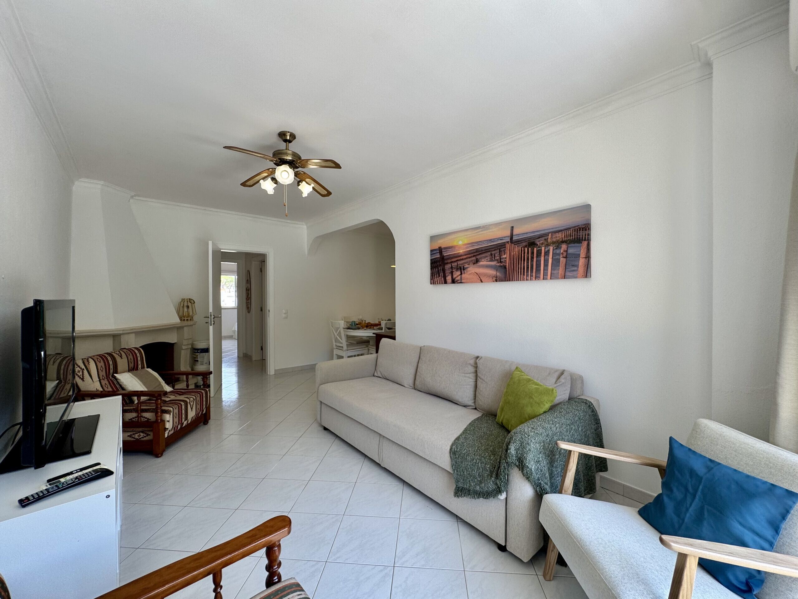 A living room with a sofa, armchairs, a television, and a ceiling fan.