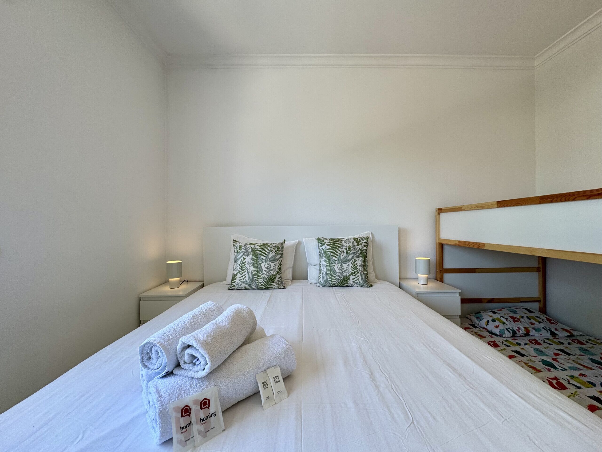 A single bed with rolled towels and a pillow, bedside lamps, and a bunk bed to the right.