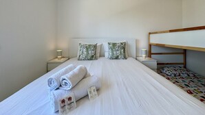 A single bed with rolled towels and a pillow, bedside lamps, and a bunk bed to the right. - VILAMOURA GOLF APARTMENT 3 WITH POOL by HOMING (Vilamoura)