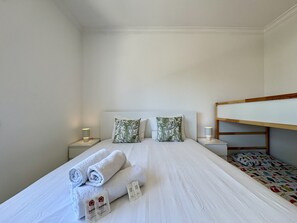Ein Einzelbett mit zusammengerollten Handtüchern und einem Kopfkissen, Nachttischlampen und ein Stockbett rechts.