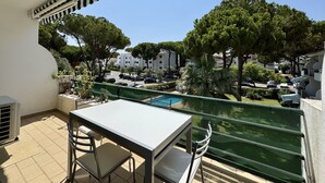 A balcony with a table and chairs, overlooking a pool and a residential area with trees and parked cars. - VILAMOURA GOLF APARTMENT 3 WITH POOL by HOMING (Vilamoura)