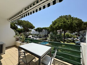 Ein Balkon mit Tisch und Stühlen, der auf einen Pool und eine Wohngegend mit Bäumen und parkenden Autos blickt.