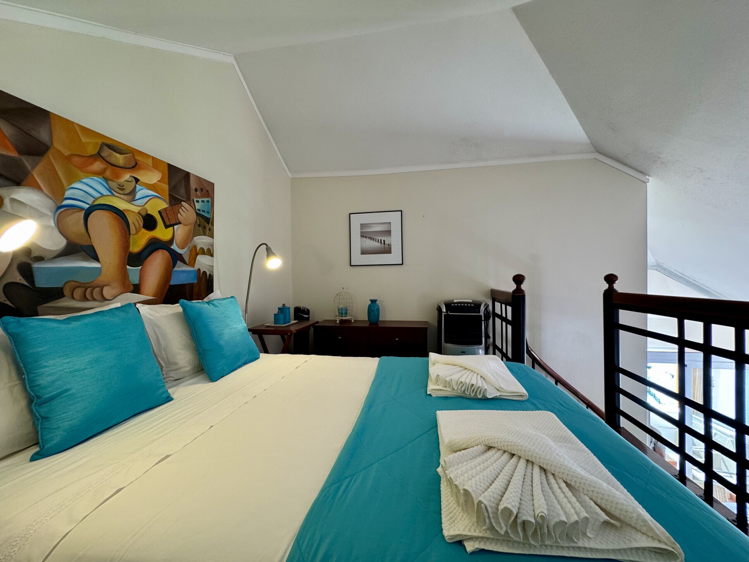 Ein Schlafzimmer mit Bett, Kissen, einer Lampe, einem Bilderrahmen, einem Heizkörper und einem Fenster.