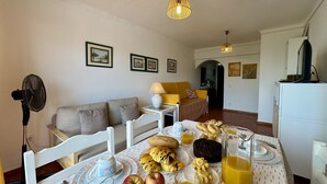 Un comedor con una mesa dispuesta para el desayuno, que incluye pan, bollería, manzanas y zumo de naranja.