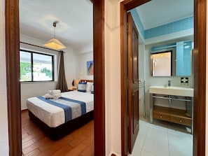 A hotel room with a bed, a window, a bathroom with a sink and mirror, and a door leading to another room. - VILAMOURA CLASSIC 3 WITH POOL by HOMING (Vilamoura)