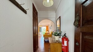 Un pasillo con extintor, puertas de madera, un espejo y un candelabro colgante.