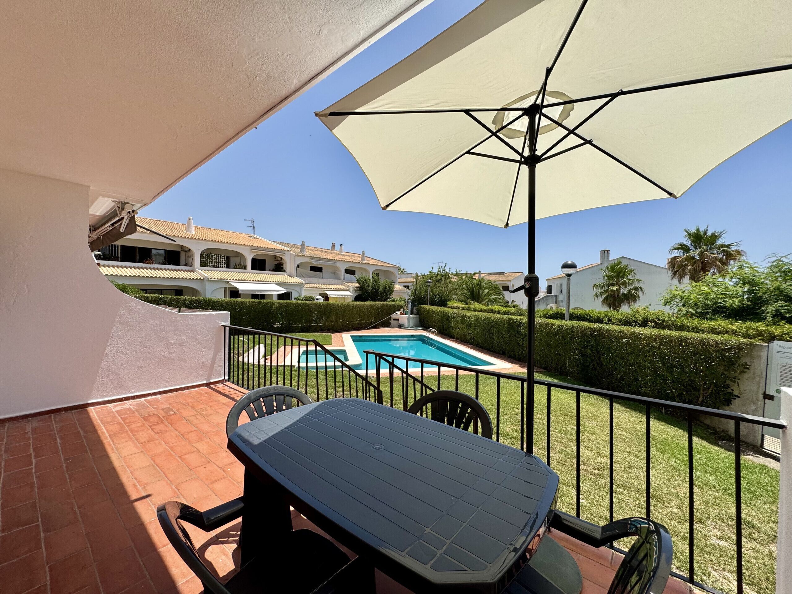 A balcony with a table and chairs, a pool, and a building in the background.