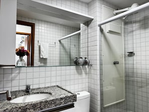 Ein Badezimmer mit Marmorwaschtisch, Toilette in Weiß, Duschkabine aus Glas und Spiegel mit Blumenvase.