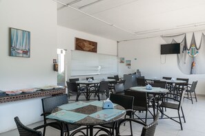 Un restaurante con mesas redondas y sillas de mimbre, un cuadro de veleros y un televisor en la pared.
