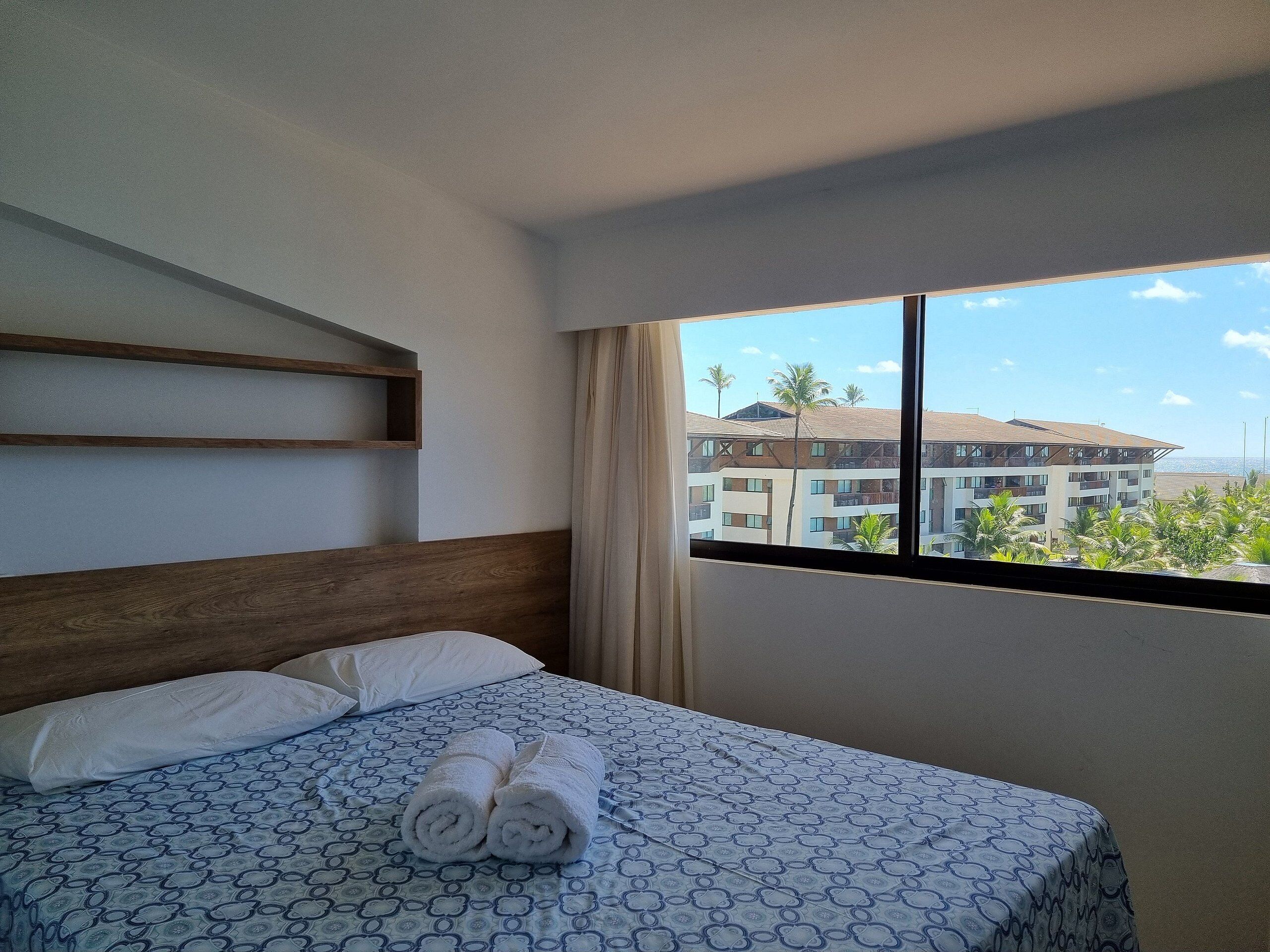 Una habitació d'hotel amb un llit, una finestra amb vista a edificis i un panell de llit de fusta.