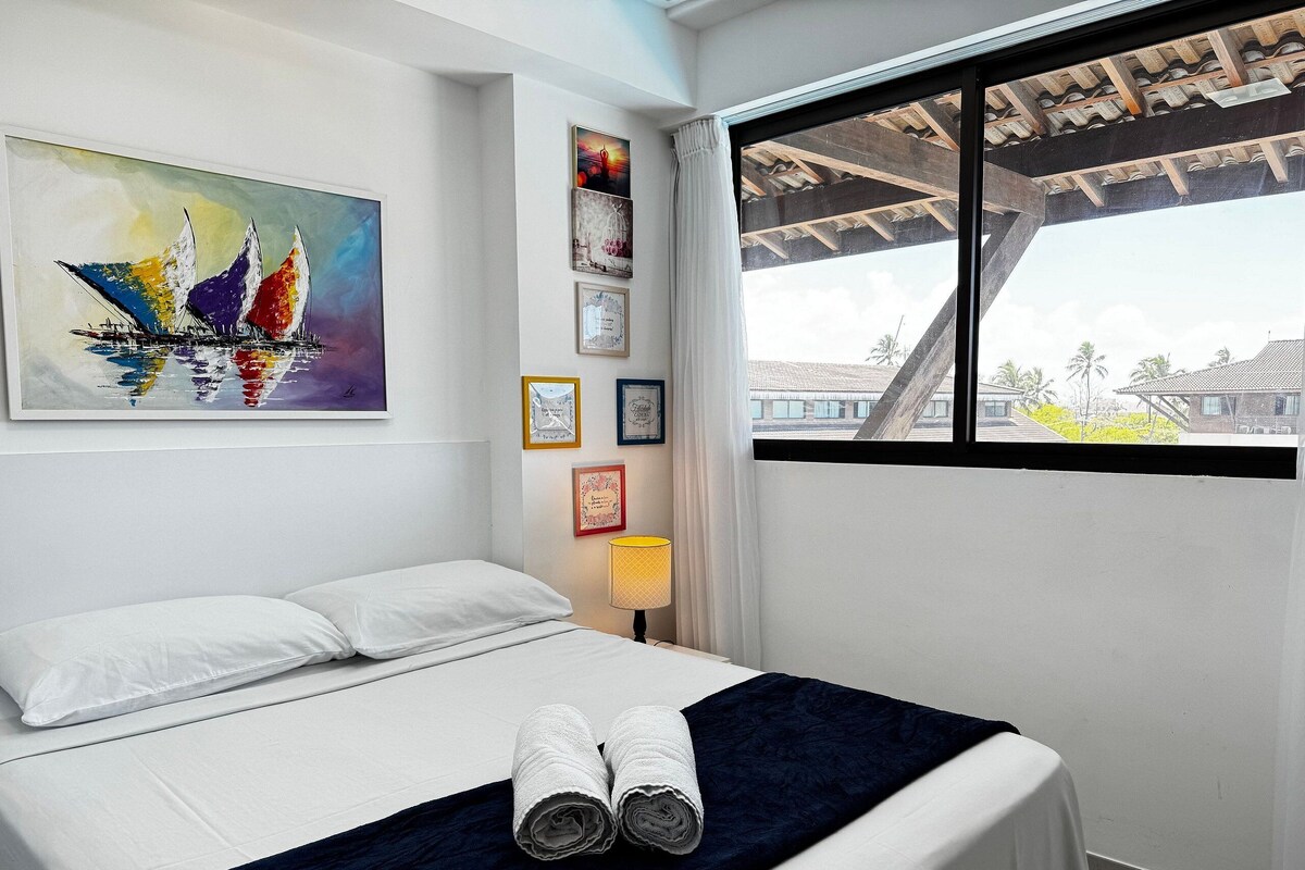 Ein Hotelzimmer mit einem Bett, einem Gemälde und einem Fenster mit Blick auf Gebäude.