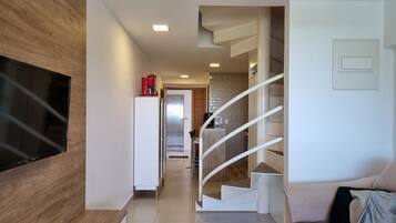 Una sala de estar moderna con un televisor de pantalla plana, una escalera y una cocina al fondo.