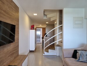 Un salon moderne avec un téléviseur à écran plat, un escalier et, au fond, un coin cuisine.