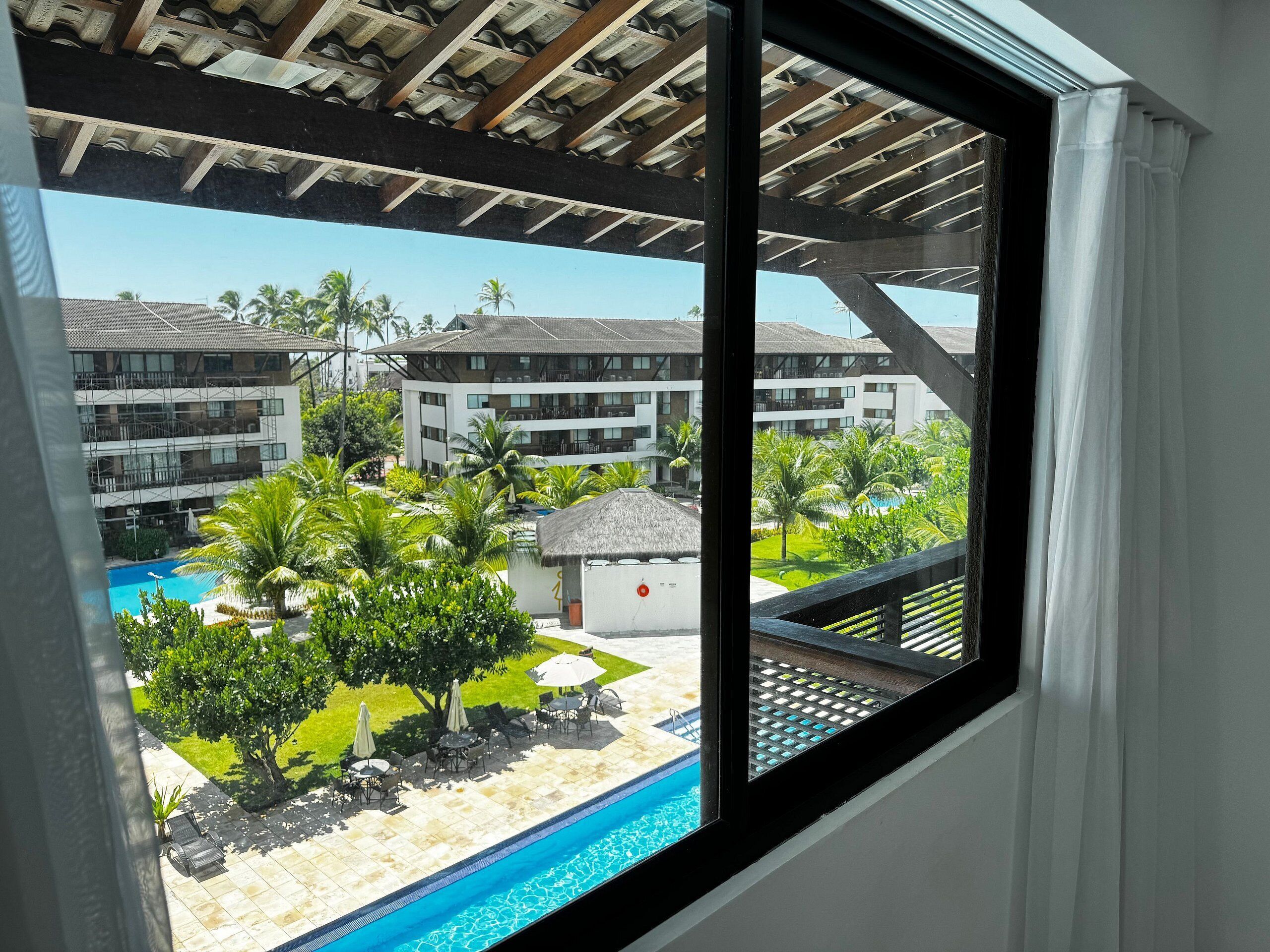 Vista de un área de piscina de hotel con cielo despejado, palmeras y un edificio con varios balcones.