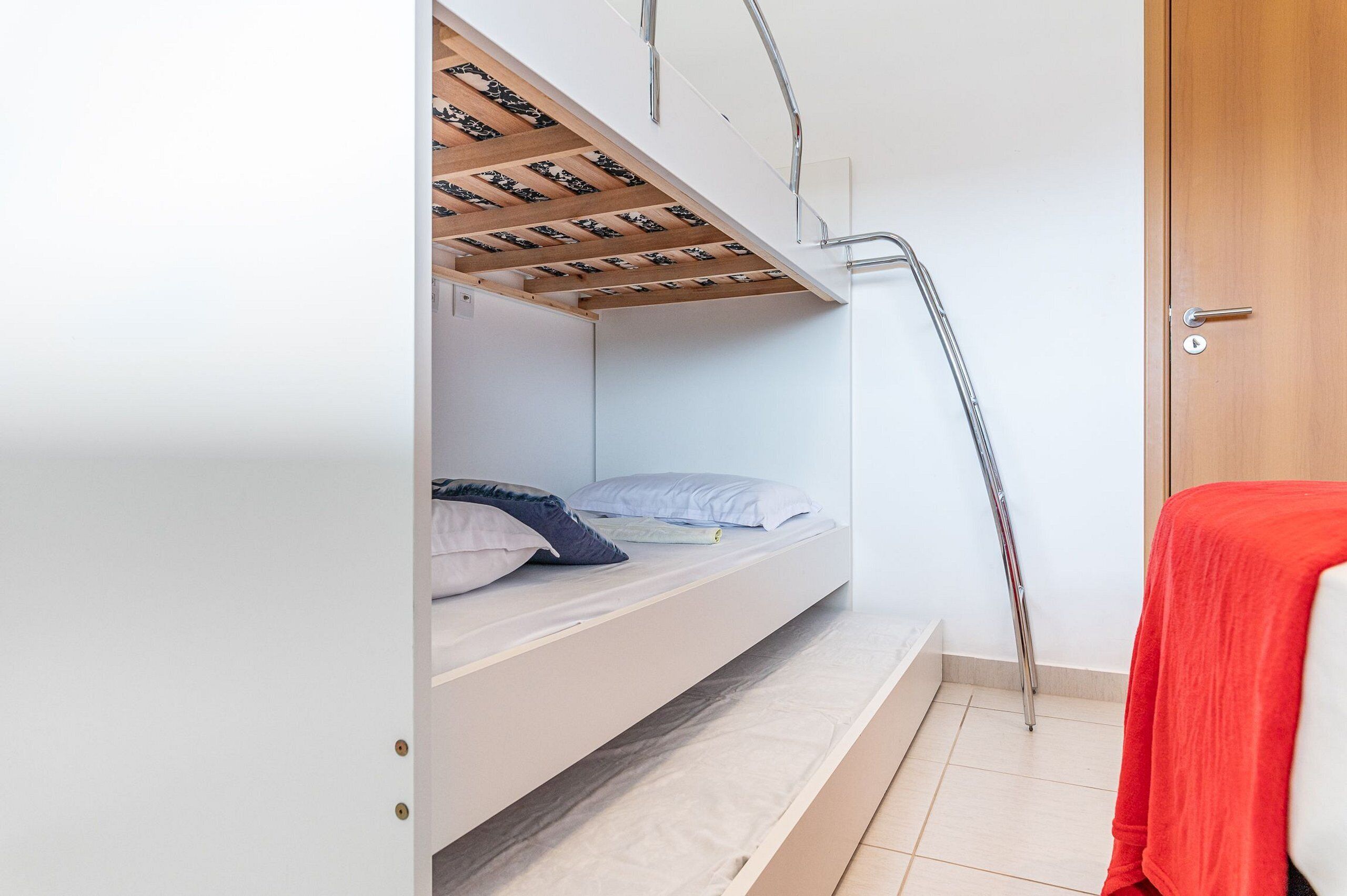 Una cama litera con una escalera de madera, una toalla roja y una puerta blanca.