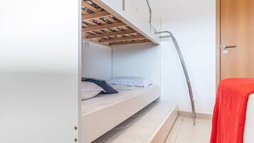 Una cama litera con una escalera de madera, una toalla roja y una puerta blanca.