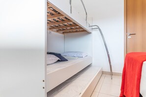 Una cama litera con una escalera de madera, una toalla roja y una puerta blanca.