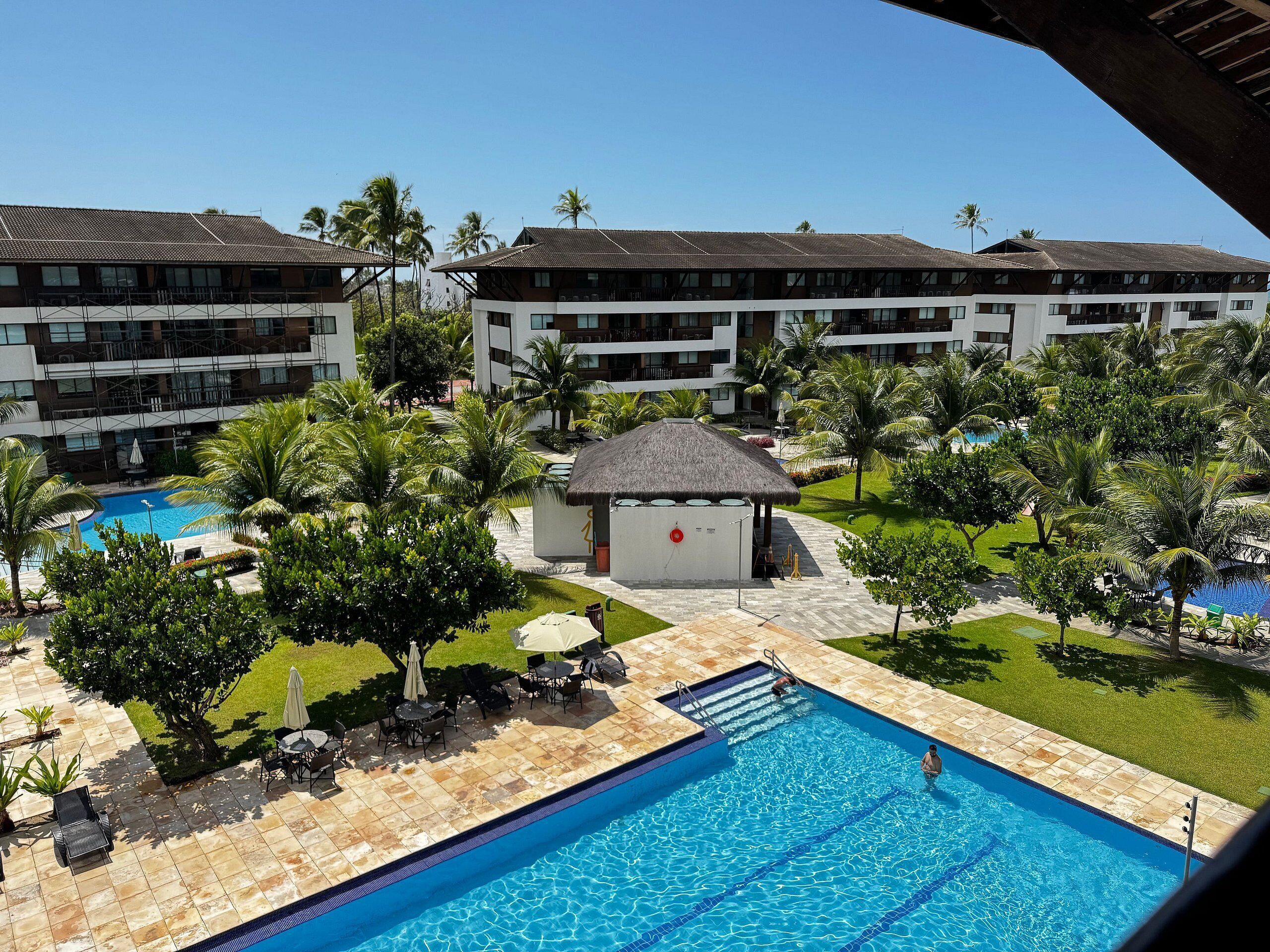 Un resort con piscina, palmeras y una estructura de techo de paja.