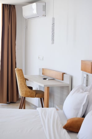 A hotel room with a bed, a desk, a chair, and an air conditioning unit.