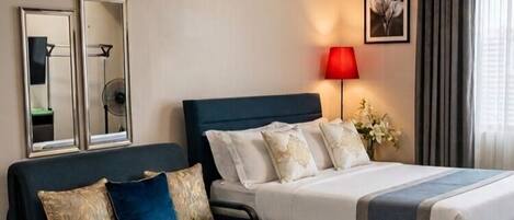 A hotel room with a bed, a sofa, a dining table with water bottles, a ceiling fan, and a lamp.