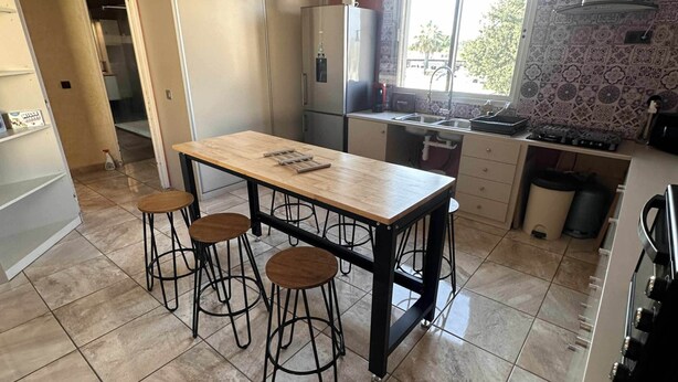 A kitchen with a central island, bar stools, a refrigerator, and a window providing natural light. - T2 tout confort avec terrasse de 30 m² et Wi-Fi – Proche plage de Canet (Canet-en-Roussillon)