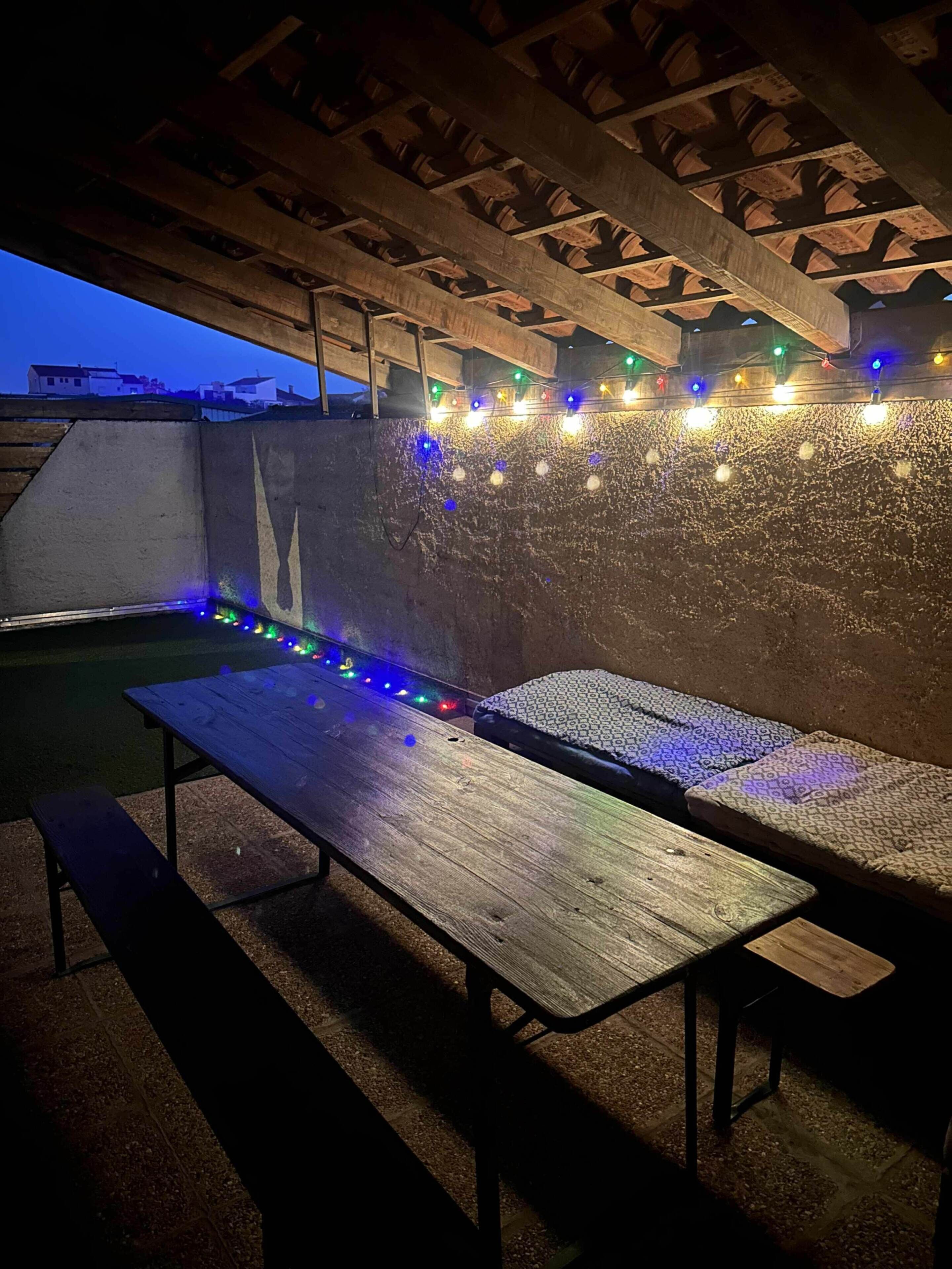 An outdoor seating area with wooden benches and a string of colorful lights.