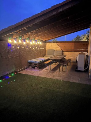 Une terrasse extérieure avec un banc en bois, une petite table et un canapé.