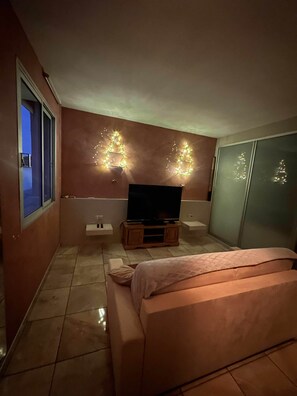 A bedroom with a bed, a TV on a wooden stand, a wall with decorative lights, and a sliding door. - T2 tout confort avec terrasse de 30 m² et Wi-Fi – Proche plage de Canet (Canet-en-Roussillon)