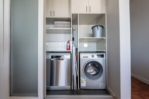 A compact laundry room with a stainless steel dishwasher, a front-loading washing machine, and a fire extinguisher on the wall. - Ocean View Apartment near V&A Waterfront (Cape Town)