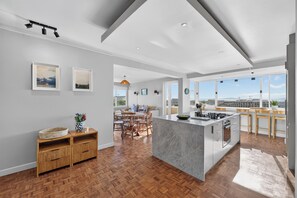 A modern kitchen with a central island, wooden flooring, and a view of the city. - Ocean View Apartment near V&A Waterfront (Cape Town)